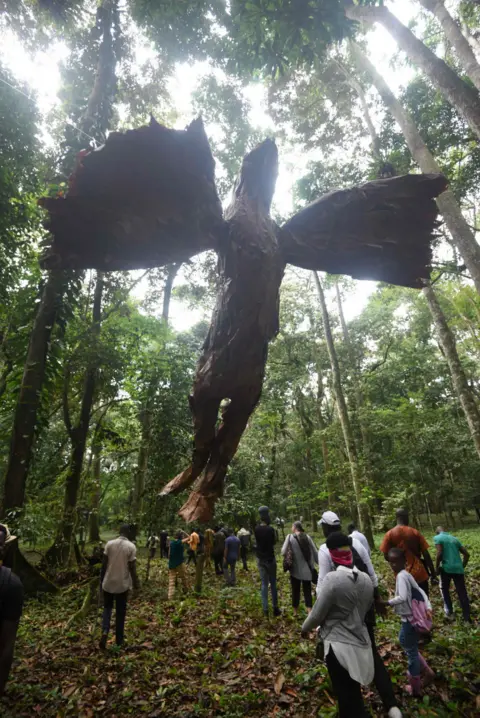 AFP People in a forest walk past a large statue hovering overhead.