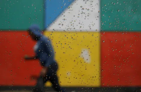 EPA A blurred figure of a woman is pictured walking past a bright mural.