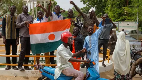 EPA Men holding up the Niger flag while a motorcycle rides past