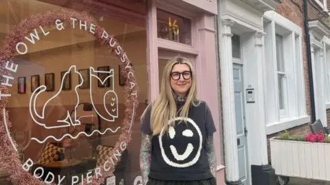 Simon Thake/BBC Woman stands in front of a pink shop front