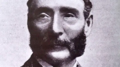 Public Domain A historic black and white photo of John Charles Shaw, who has a mutton chops style of beard.