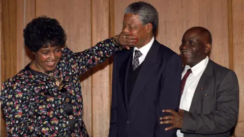 PA Wire Nelson Mandela is playfully silenced by Winnie Mandela as they leave a London press conference in 1990