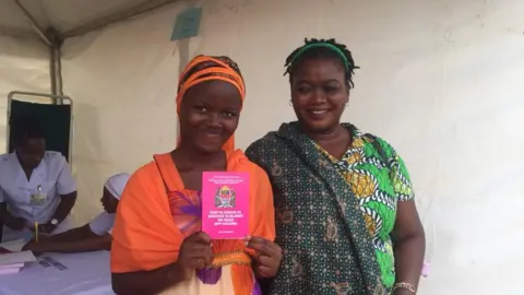 BBC A girl who has been immunised poses with her vaccination booklet