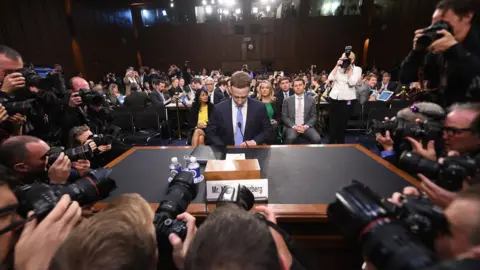 Getty Images Mark Zuckerberg looks down as he takes his seat in the committee chamber, surrounded by a ring of photographers pressing in around him