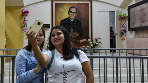 AFP Two women take a selfie with a portrait of Archbishop Oscar Romero