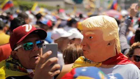 Reuters A man wearing a mask caricaturing US President Donald Trump poses for a selfie during a rally against Venezuelan President Nicolas Maduro's government in Caracas, February 2, 2019