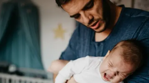 Getty Images/Anchiy Father holding crying baby
