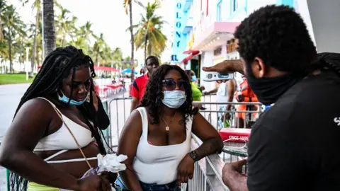 Getty Images A security guard checks the temperature of a woman at the entrance of a restaurant on Ocean Drive in Miami Beach, Florida, 24 June 2020