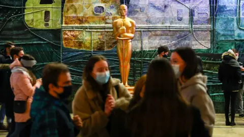 Getty Images Cinema fans in masks in front of an Oscars statue