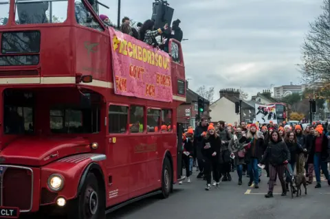 Getty Images Anti-Boris Johnson protesters walk behind a red bus