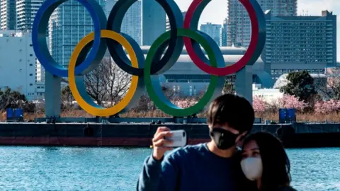 Getty Images A couple take a selfie in front of the Olympic rings on display at the Odaiba waterfront in Tokyo