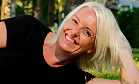 Hollie McFarlane A photo of Hollie laying on the grass outside smiling with long blonde hair before her cancer diagnosis