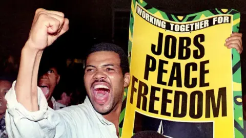 AFP A coloured (mixed race) supporter shouts pro-Nelson Mandela slogans while holding a ANC election manifesto poster here at an election campaign meeting in Promosa, a coloured township outside Potchefstroom in western Transvaal, South Africa, 30 January 1994.