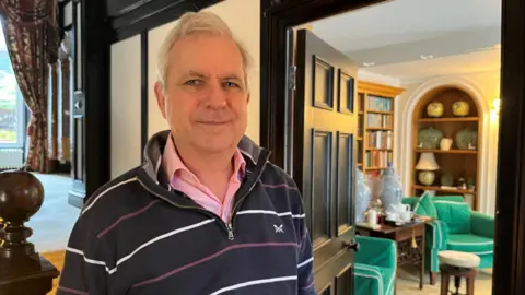 A man standing beside a doorway smiling at the camera
