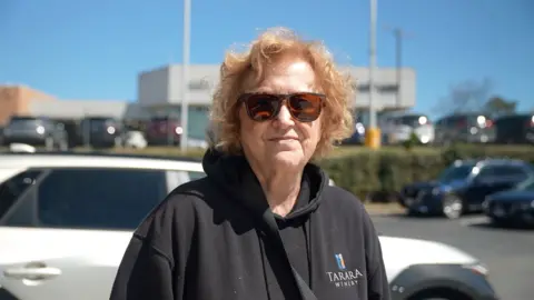 Woman stands with sunglasses and balck sweatshirt