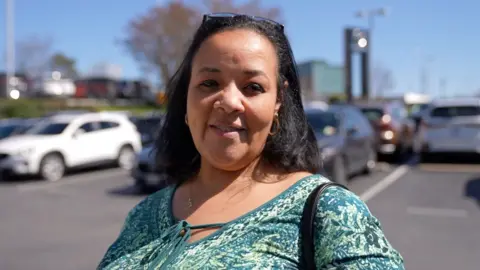 Woman with long black hair looks at camera in car park