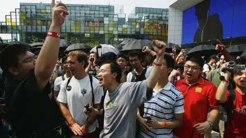 Getty Images Customers celebrate as they wait to enter the first Apple store on July 19, 2008 in Beijing. The photos shows a group of men in t-shirts shouting and cheering.