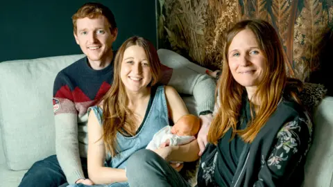 PA Media Transplant UK of Grace and Angus Davidson with baby Amy Isabel, and her aunt Amy (right). Grace Davidson who received a womb in the UK's first womb transplant has given birth to a baby girl.