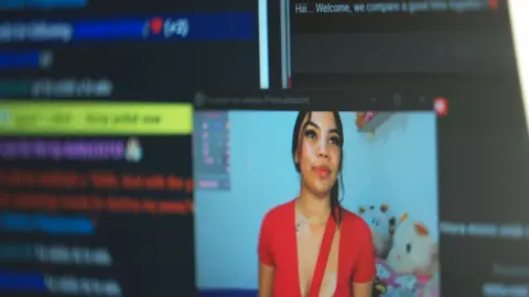 A computer screen - in the bottom right corner is a young woman with dark hair, in a red top, and the rest of the screen is covered in typed messages. 