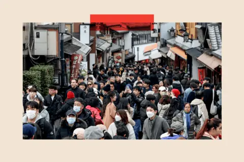 Getty Images Busy crowds of tourists holding up phones and wearing Covid masks on a narrow, crowded street