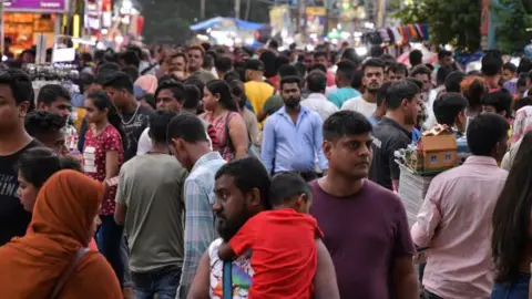 Getty Images A man holding a child speaks to a woman amid a large crowd in Kolkata, India.