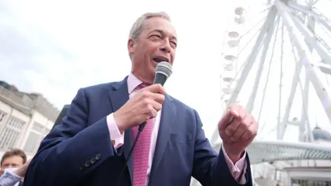 PA Media Nigel Farage addresses crowds in Clacton, with microphone in hand and ferris wheel in the background