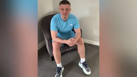 Supplied Image of Dale Martin. He is sat on a chair and is wearing a sky blue t-shirt and shorts.
