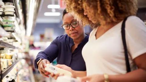 Getty Images Two women look at the price of cheese in a supermarket chilled dairy aisle.